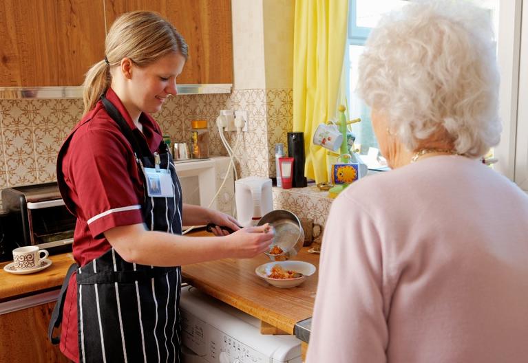 Home health worker preparing food for an older woman standing nearby